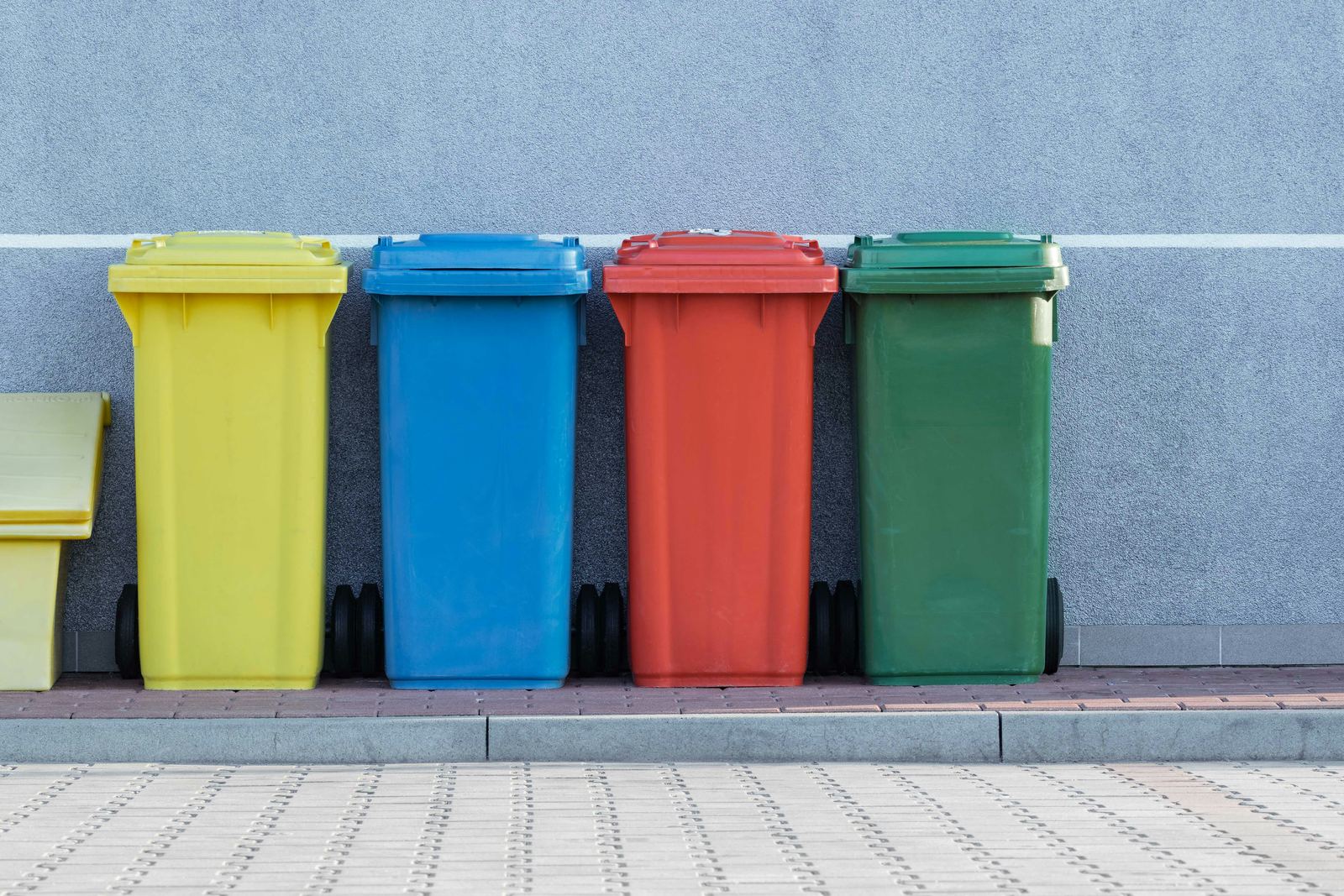 Four colour-coded wheeled bins in yellow, blue, red and green standing in a row against a clean wall.
