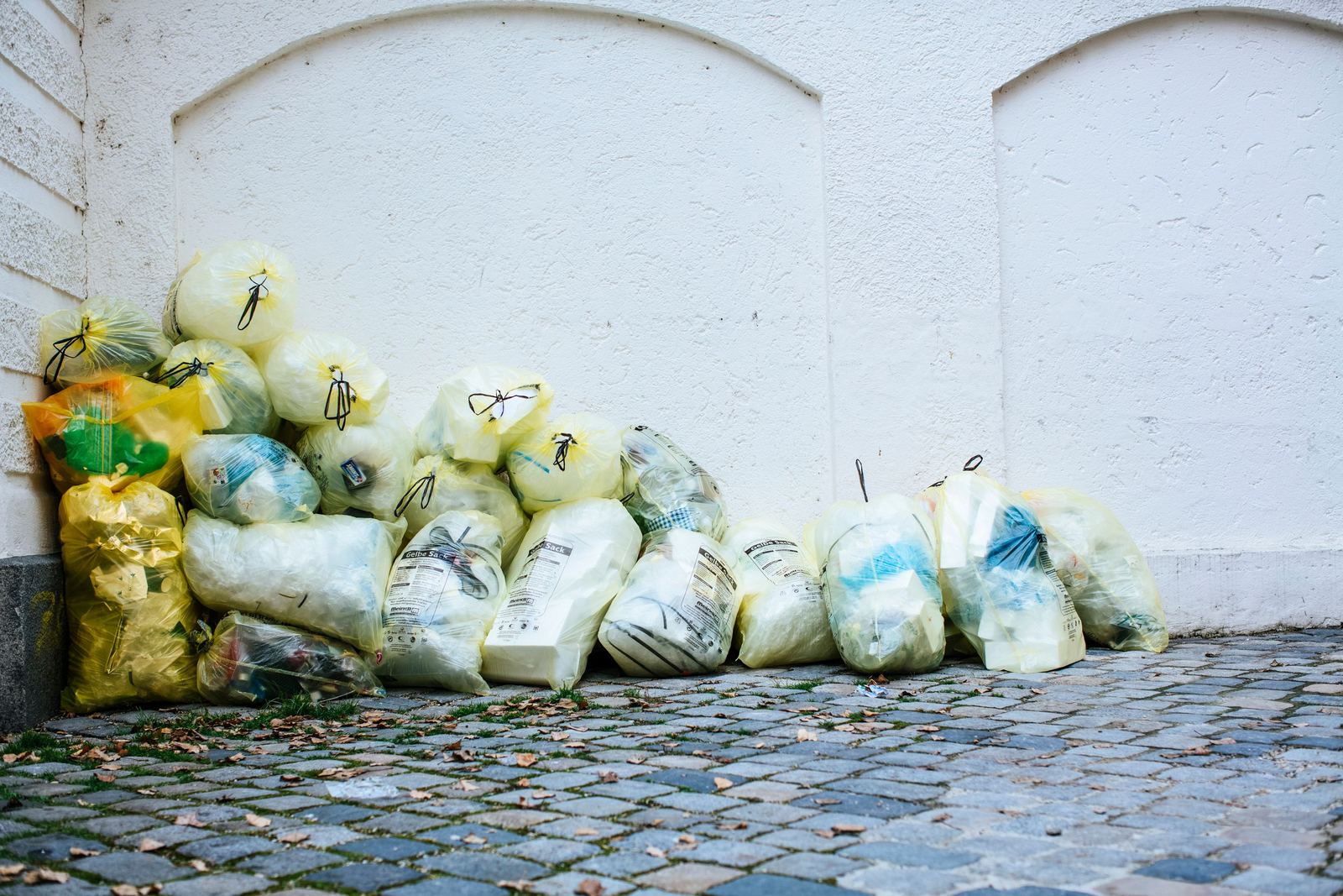 A pile of tied plastic refuse sacks stacked against a building wall on a cobbled service street.
